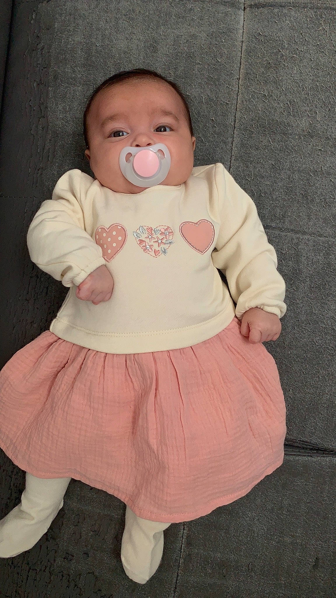 Maëlys participe au concours pour gagner de l'argent avec cette photo : abdomen, arm, baby, baby_products, baby_toddler_clothing, bib, cheek, child, eye, iris, neck, pattern, peach, person, pink, ruffle, skin, sleeve, t_shirt, toddler