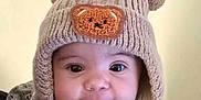 Winter is registered to the contest to win money with this photo: baby, child, knitted_hat, bear_patch, cute, smiling, portrait, indoor, clothing, ruffles, infant, face, headwear, warm_clothing, adorable, person, young_child, happy, closeup, soft_lighting