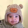 baby, child, knitted_hat, bear_patch, cute, smiling, portrait, indoor, clothing, ruffles, infant, face, headwear, warm_clothing, adorable, person, young_child, happy, closeup, soft_lighting