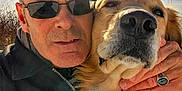 Siri is registered to the contest to win money with this photo: man, dog, golden_retriever, selfie, outdoor, sunlight, sunglasses, portrait, face, hand, ring, fur, pet, animal, closeup, nature, sky, casual, warm_light, affection