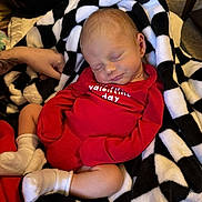 Kash joined the competition — help win amazing prizes! baby, newborn, sleeping, blanket, red_clothing, onesie, white_socks, tattoo, hand, indoor, cozy, comfort, peaceful, infant, cute, soft, rest, black_and_white, checkered_pattern, portrait