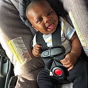 Dhovonni is registered to the contest to win money with this photo: baby, black_hair, car_interior, car_seat, casual_wear, child, clothing, cute, happy, head_support, indoors, infant, joyful, person, safety_harness, seatbelt, small_hands, smile, sock, young_child