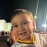child, smiling, face, portrait, night, outdoor, people, crowd, lights, happy, clothing, striped_shirt, young_child, casual, closeup, person, background, event, fun, cute