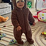 toddler, child, onesie, bear_costume, hat, indoor, living_room, rug, toy_car, stuffed_animal, floor, curious, baby, footwear, play_area, furniture, cozy, smile, person, home