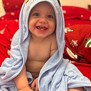Arian joined the competition — help win amazing prizes! baby, child, towel, blue_towel, hooded_towel, smiling, happy, bare_chest, red_bedspread, snowflake_pattern, indoors, cute, infant, sitting, small_hands, soft_texture, cozy, portrait, face, playful