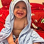 baby, child, towel, blue_towel, hooded_towel, smiling, happy, bare_chest, red_bedspread, snowflake_pattern, indoors, cute, infant, sitting, small_hands, soft_texture, cozy, portrait, face, playful