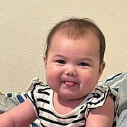 Harlee is registered to the contest to win money with this photo: baby, child, face, tongue, striped_shirt, arm, pillow, blanket, smile, cheeks, infant, sitting, cute, indoors, person, young_child, skin, hair, happy, portrait