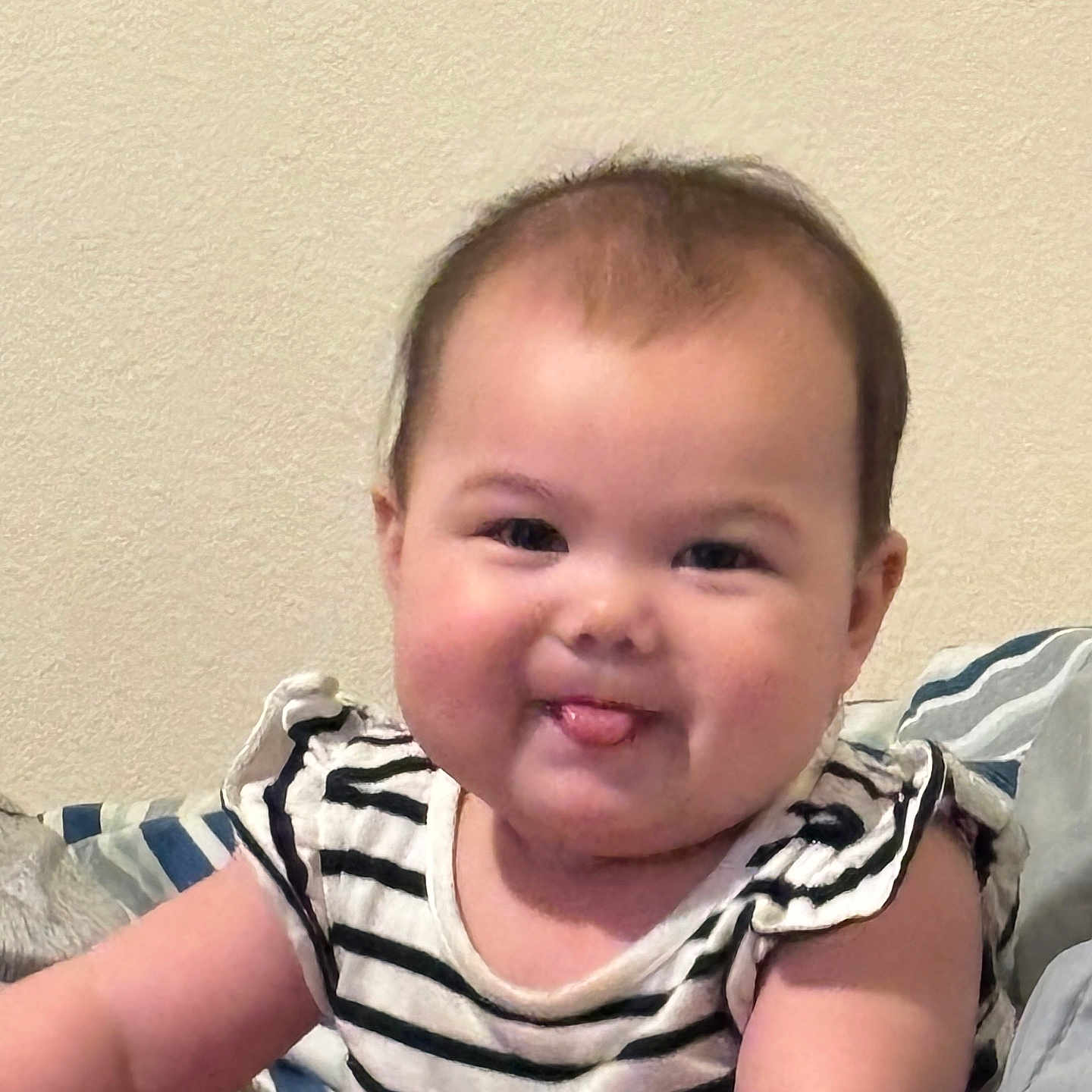 Harlee is registered to the contest to win money with this photo: arm, baby, blanket, cheeks, child, cute, face, hair, happy, indoors, infant, person, pillow, portrait, sitting, skin, smile, striped_shirt, tongue, young_child