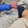 newborn, baby, hospital, swaddled, blanket, hat, gloved_hand, person, tattoo, arm, bed, medical, resting, infant, sleeping, closeup, healthcare, patient, care, indoors