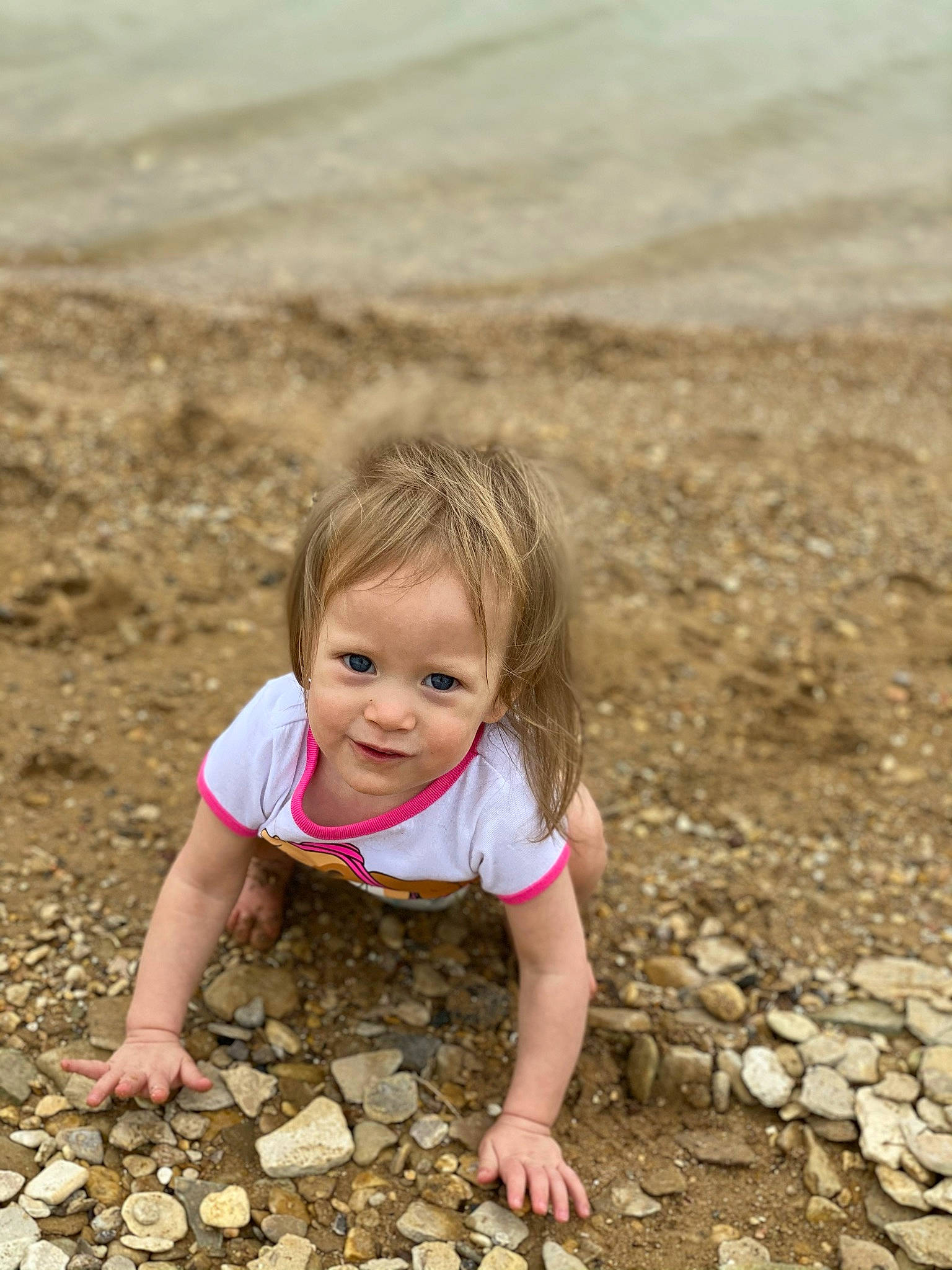 Skye is registered to the contest to win money with this photo: beach, blond, body_of_water, eye, face, flooring, fun, grass, hair, happy, head, landscape, leisure, natural_environment, people_in_nature, person, road_surface, sand, sitting, toddler