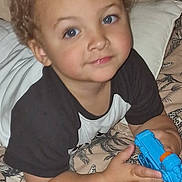 Lyrico is registered to the contest to win money with this photo: child, toddler, curly_hair, blue_eyes, toy_gun, bed, blanket, pattern, animal_print, pillow, black_and_white_shirt, smile, face, hand, indoor, cute, lying_down, playing, young_child, person