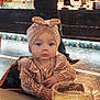 baby, child, infant, headband, striped_clothing, table, glass, orange_juice, drink, indoor, person, adult, blurred_background, restaurant, food, casual_clothing, seated, cute, portrait, cozy
