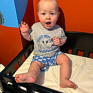 Xaiden joined the competition — help win amazing prizes! baby, child, toddler, sitting, shirt, shorts, expression, mouth_open, furniture, changing_table, wall, orange, blue, foot, hand, person, indoor, clothing, face, skin