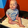 baby, child, infant, toddler, sitting, crib, mattress, grey_tshirt, text_on_clothing, blue_eyes, blond_hair, indoor, orange_wall, blue_wall, cute, chubby_cheeks, hand, foot, smile, casual_clothing