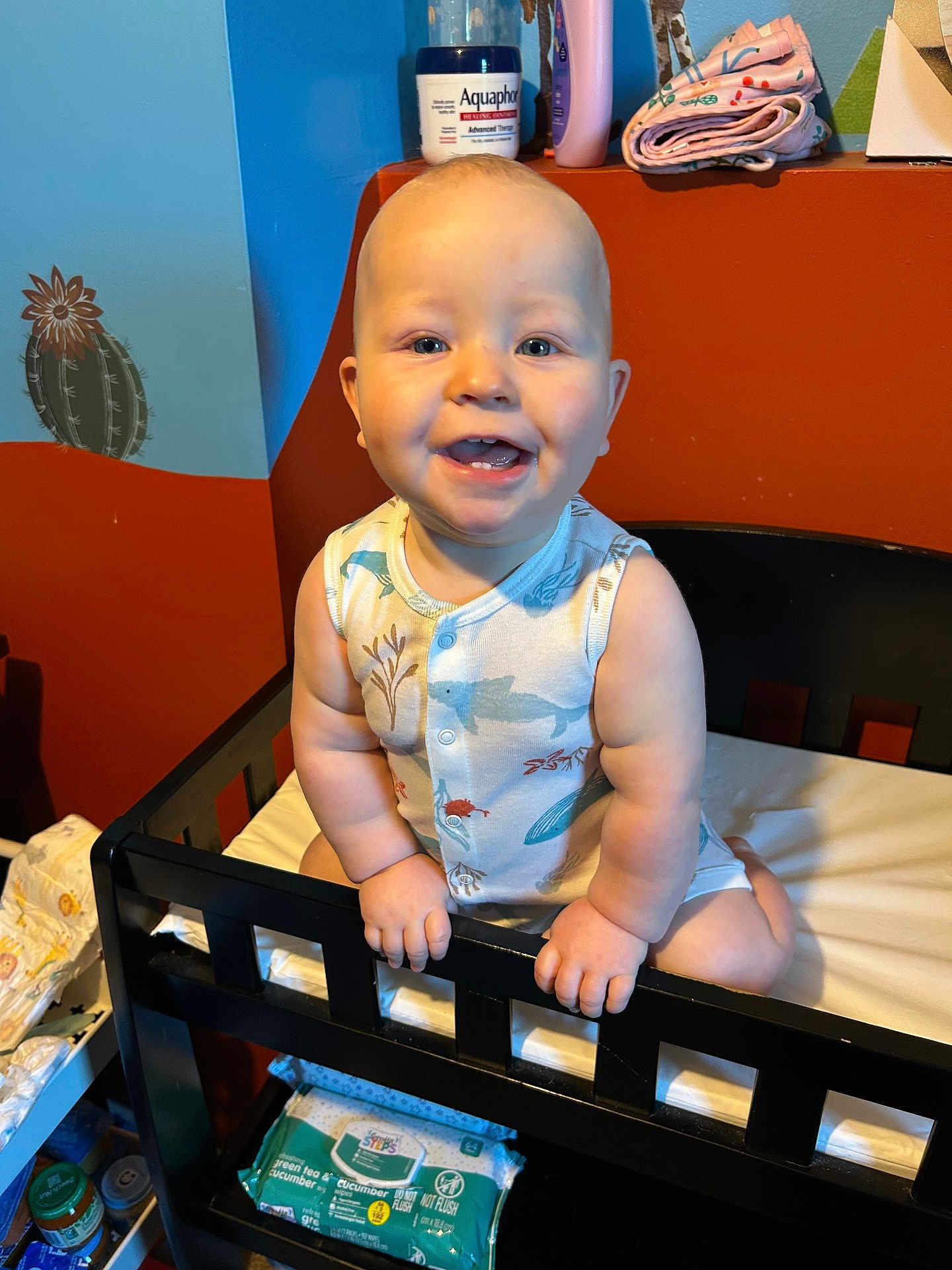 Xaiden joined the competition — help win amazing prizes! baby, smiling, crib, nursery, child, indoor, sitting, happy, face, clothing, baby_care, shelf, wall_art, cactus, bottle, container, diapers, person, infant, room