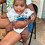 baby, child, person, toddler, adult, clothing, shirt, diaper, chair, hand, foot, outdoor, concrete, door, wall, sitting, smiling, playful, holding, casual