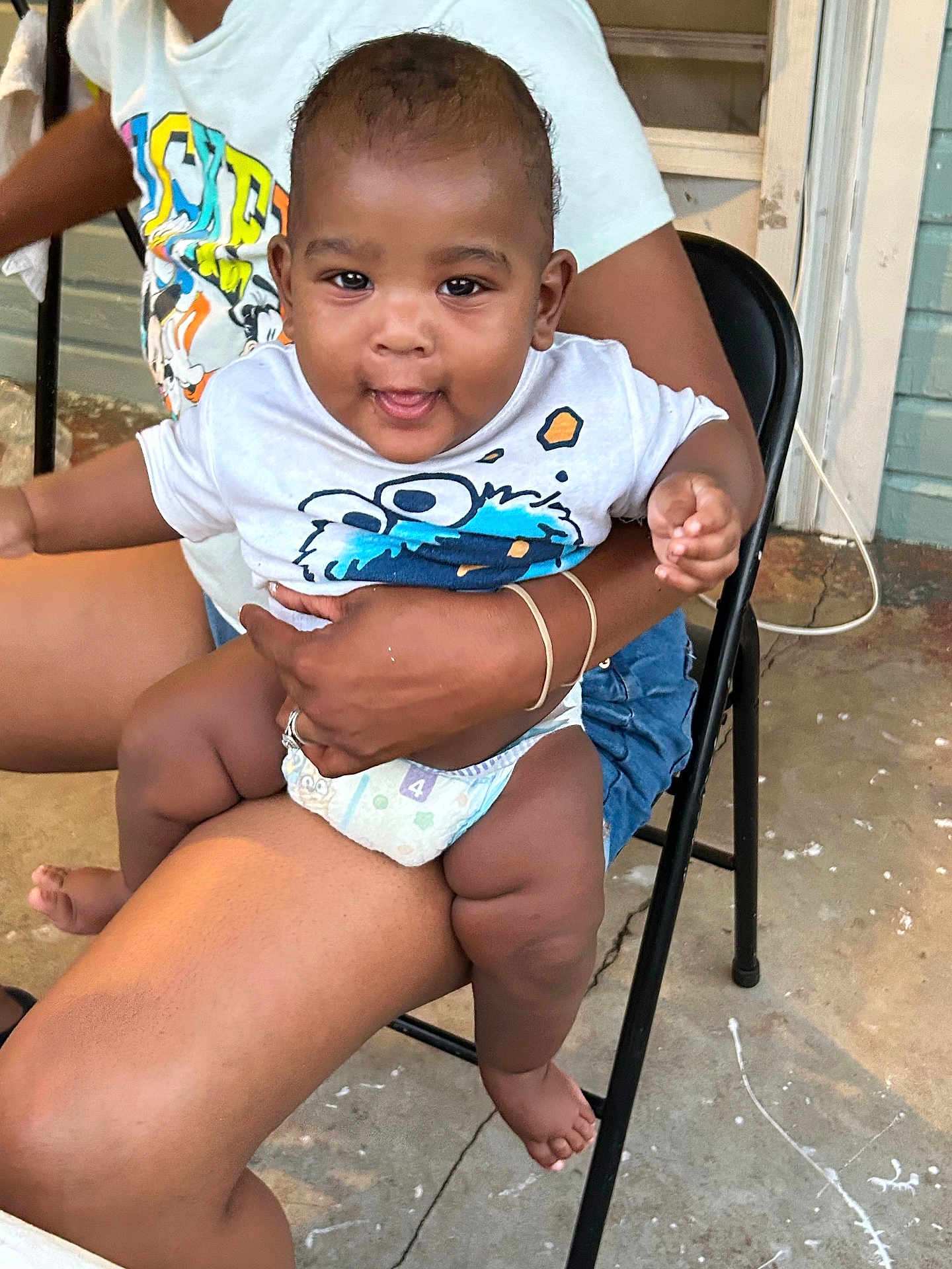 Robert is registered to the contest to win money with this photo: baby, child, person, toddler, adult, clothing, shirt, diaper, chair, hand, foot, outdoor, concrete, door, wall, sitting, smiling, playful, holding, casual