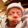 newborn, baby, infant, hospital, medical_tube, nasal_cannula, striped_cap, blanket, sleeping, face, closeup, skin, person, child, healthcare, indoors, soft_lighting, wrapped, cute, peaceful