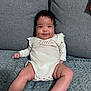 Olivia is registered to the contest to win money with this photo: baby, infant, smile, curly_hair, onesie, couch, blanket, chubby_cheeks, cute, sitting, indoors, child, person, happy, portrait, young, skin, comfortable, cozy, expression