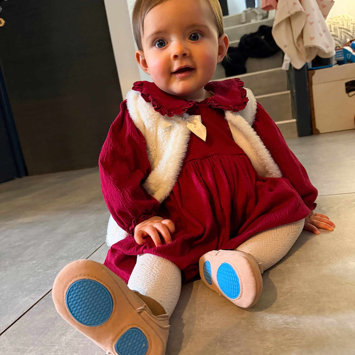 Lola a rejoint le concours — aidez-le/la à gagner de superbes lots ! baby, blue_sole_shoes, child, clothing, curious, cute, floor, floor_tiles, home_interior, indoor, person, portrait, red_dress, sitting, smiling, stairs, toddler, warm_lighting, white_vest, young_child
