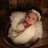 Kaylani is registered to the contest to win money with this photo: baby, child, cozy, cute, expression, face, flower_crown, fluffy_cushion, headband, indoor, infant, newborn, person, portrait, skin, soft_texture, swaddled, wooden_bucket, wooden_floor, wrapped
