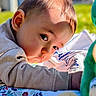 baby, child, infant, face, skin, hair, clothing, sleeve, blanket, pattern, toy, plush, green, outdoor, grass, daylight, portrait, curious, lying_down, closeup