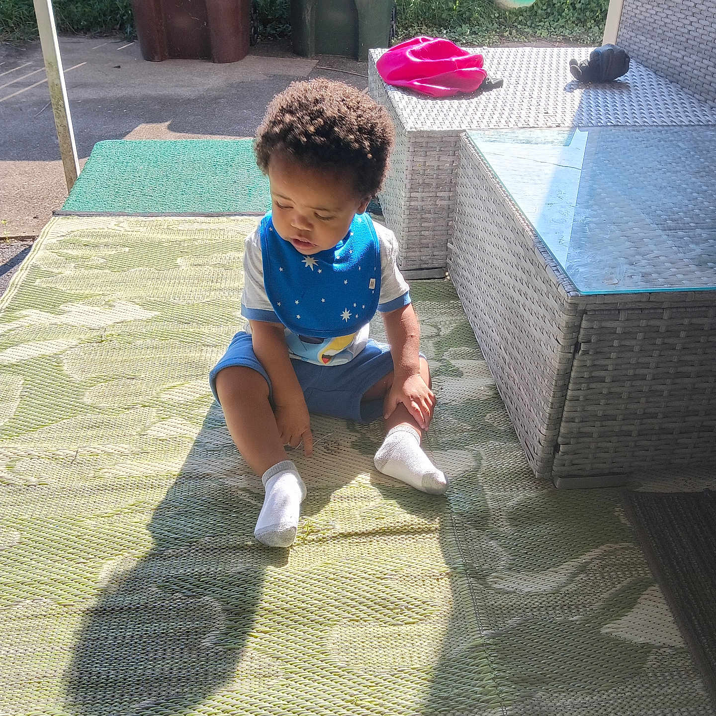 Diamond joined the competition — help win amazing prizes! toddler, child, outdoor, sunlight, shadow, bib, socks, rug, patio_furniture, table, chair, trash_bins, fence, grass, concrete, curious, sitting, blue_clothing, daylight, backyard