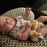 baby, infant, smiling, plush_toy, cushion, patterned, clothing, indoor, cute, lying_down, child, person, soft_toy, relaxed, happy, small_hands, head, face, eyes, cozy