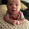 Dylan is registered to the contest to win money with this photo: baby, infant, face, eyes, mouth, hands, pillow, pattern, clothing, red_trim, indoor, soft_light, curious, expression, close_up, couch, blurred_background, skin, head, person