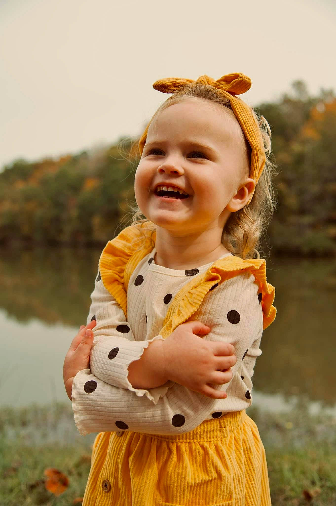 Mercedez is registered to the contest to win money with this photo: baby, baby_toddler_clothing, blond, child, eye, face, fun, grass, happy, head, joy, lake, orange, people_in_nature, person, plant, sky, sleeve, smile, toddler