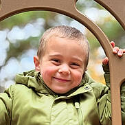 Lorenzo joined the competition — help win amazing prizes! child, boy, smiling, green_jacket, outdoor, playground, hand, face, portrait, happy, winter_clothing, hooded_jacket, nature, tree, blurred_background, young, cute, casual, person, daylight