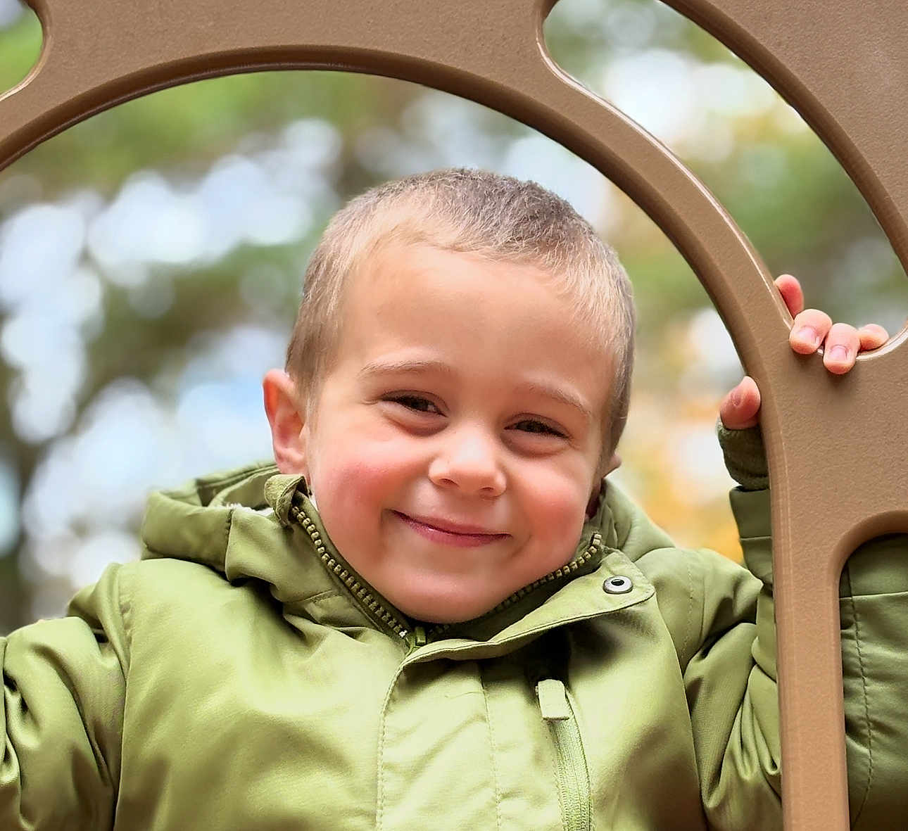Lorenzo joined the competition — help win amazing prizes! child, boy, smiling, green_jacket, outdoor, playground, hand, face, portrait, happy, winter_clothing, hooded_jacket, nature, tree, blurred_background, young, cute, casual, person, daylight