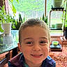 Lorenzo is registered to the contest to win money with this photo: child, smiling, indoor, plants, window, table, pot, greenery, face, happy, portrait, young_boy, casual_clothing, natural_light, home, carpet, potted_plants, furniture, background, closeup