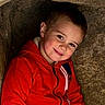 Lorenzo is registered to the contest to win money with this photo: child, boy, smile, red_hoodie, stone, alcove, portrait, face, young, casual_clothing, cozy, happy, cute, outdoor, natural_light, texture, warm_colors, playful, person, headshot