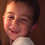 Lorenzo is registered to the contest to win money with this photo: child, boy, smiling, laughing, portrait, indoors, wooden_wall, warm_lighting, short_hair, white_shirt, face, head, shoulders, close_up, happy, joyful, photograph, sitting, casual, expression