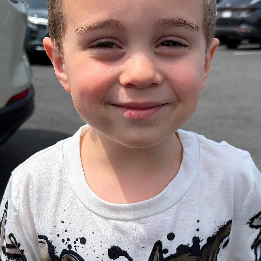 Lorenzo is registered to the contest to win money with this photo: child, boy, smiling, tshirt, outdoor, parking_lot, daylight, short_hair, face, person, casual_clothing, standing, young, happy, urban, vehicle, asphalt, background, expression, portrait