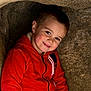 child, boy, red_hoodie, smile, face, portrait, rock, cave, outdoor, casual_clothing, young, happy, cute, cozy, natural_light, head_and_shoulders, brown_hair, eyebrows, cheeks, zipper