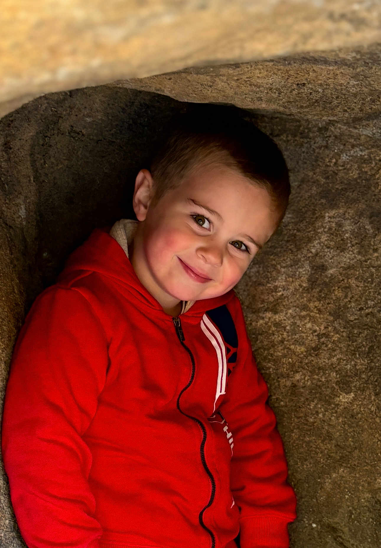 Lorenzo joined the competition — help win amazing prizes! child, boy, red_hoodie, smile, face, portrait, rock, cave, outdoor, casual_clothing, young, happy, cute, cozy, natural_light, head_and_shoulders, brown_hair, eyebrows, cheeks, zipper