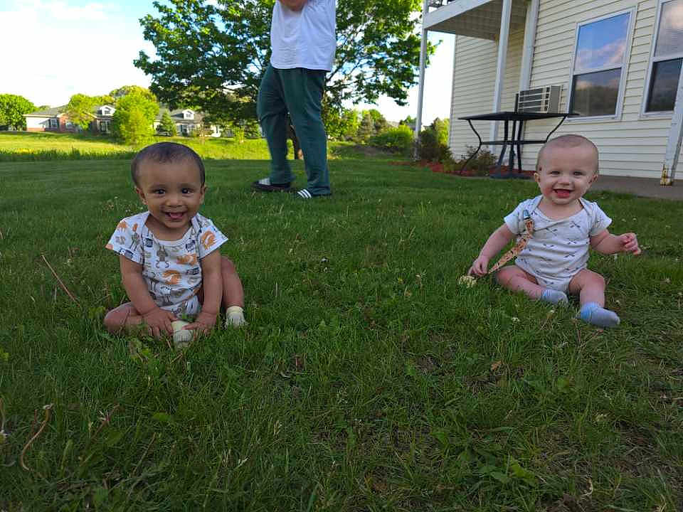 Junior And Jaxton is registered to the contest to win money with this photo: baby, grass, outdoor, smiling, child, house, person, greenery, sunny_day, sitting, happy, footwear, table, window, air_conditioner, clothing, nature, yard, daytime, playful