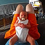 baby, pacifier, person, legs, orange_shorts, white_onesie, living_room, television, furniture, couch, carpet, basket, clothing, indoor, home, child, sitting, hands, face, relaxation