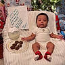 Tayloure is registered to the contest to win money with this photo: baby, infant, child, christmas, christmas_tree, presents, gift_wrapping, ornaments, festive, holiday, sitting, chair, blanket, white_onesie, red_socks, smiling, portrait, cookies, note, indoor