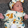 baby, infant, child, portrait, lying_down, headband, bow, onesie, patterned_clothing, dinosaur, giraffe, fuzzy_blanket, gray_blanket, indoors, face, hands, feet, white_sock, awake, cute