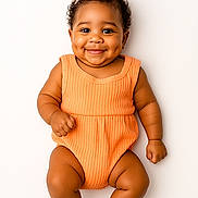 Ocean-Sinclair joined the competition — help win amazing prizes! baby, infant, smiling, dimples, curly_hair, bow, orange_onesie, socks, cute, portrait, happy, child, young, studio, white_background, skin, face, person, baby_clothing, sitting