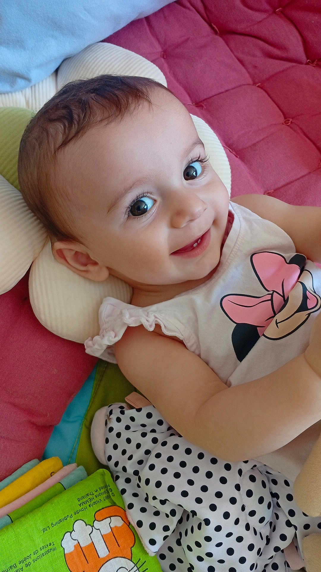 Gabie a rejoint le concours — aidez-le/la à gagner de superbes lots ! baby, child, smiling, face, eyes, clothing, minnie_mouse, toy, blanket, pillow, cushion, polka_dot, infant, cute, portrait, happy, lying_down, indoors, soft_toy, colorful