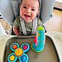 James joined the competition — help win amazing prizes! baby, high_chair, toy, smile, child, playtime, colorful, happy, infant, seatbelt, face, indoors, wooden_floor, cute, person, plastic_toy, sitting, bright, cheerful, expression