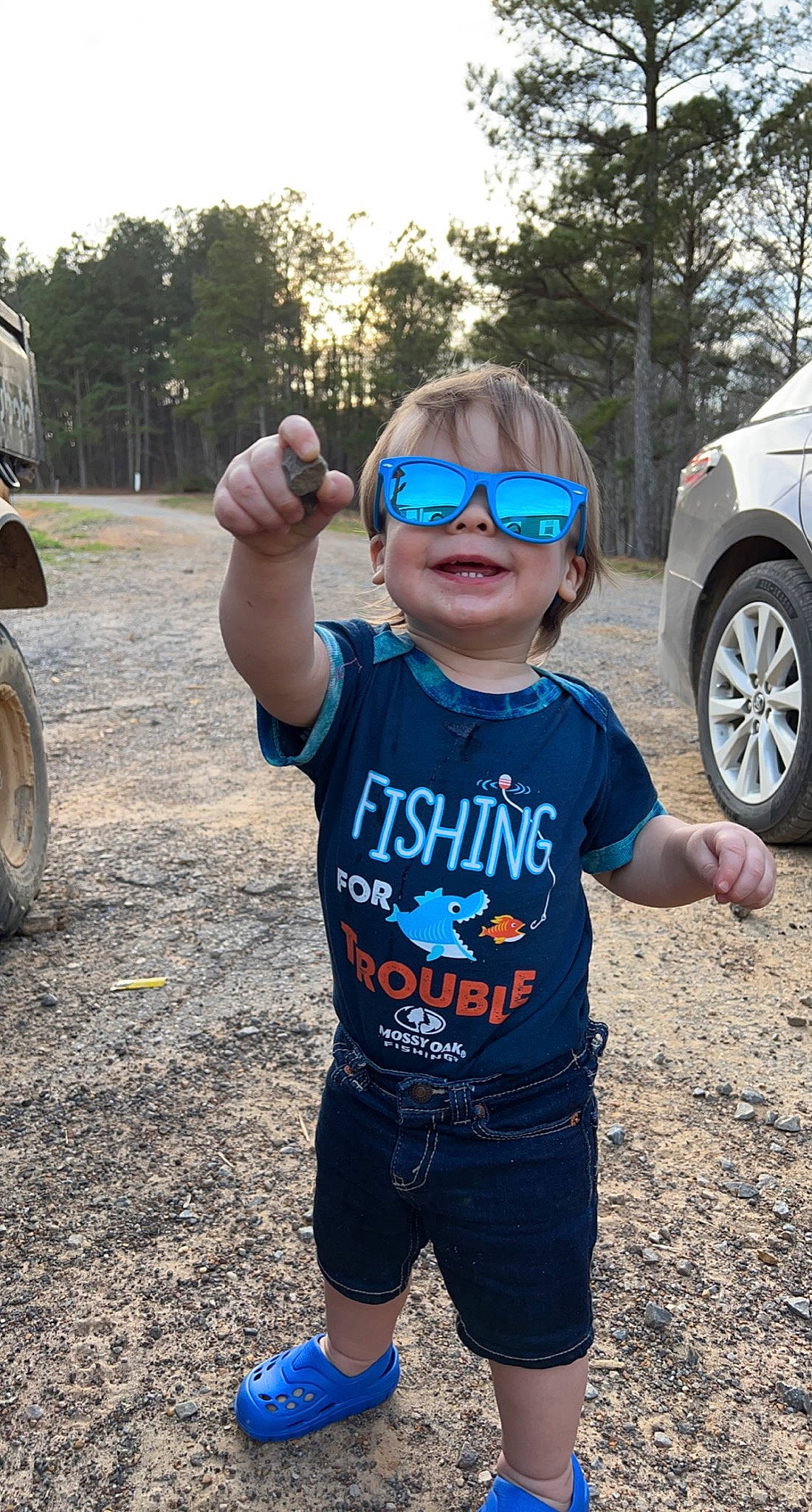 Bryer is registered to the contest to win money with this photo: automotive_tire, blue, car, cool, eyewear, finger, gesture, glasses, goggles, happy, person, plant, sleeve, smile, sunglasses, tire, toddler, tree, vehicle, vision_care