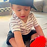 Rayshan is registered to the contest to win money with this photo: toddler, child, cap, black_cap, striped_shirt, shorts, toy, red_toy, bracelet, indoors, living_room, couch, window, natural_light, playing, sitting, curious, person, young_child, casual_clothing