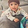 baby, child, infant, hat, onesie, animal_print, couch, sofa, pillow, indoor, toy, inflatable, curious, lying_down, cozy, cute, face, hand, expression, soft_furniture