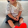 toddler, child, cap, striped_shirt, shorts, red_shoes, bracelet, earrings, couch, indoor, curious, sitting, cute, face, footwear, casual_clothing, portrait, young_child, home, bright_colors
