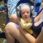 Chance is registered to the contest to win money with this photo: adult, baby, bed, blanket, clothing, curious, expression, floor, footwear, furniture, head, headphones, holding, indoor, legs, messy, person, room, sitting, skin